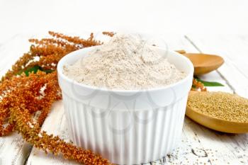 Flour amaranth in a bowl, a spoon with grain, brown flower with green leaves on a background of wooden boards