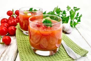 Gazpacho tomato soup in two glasses with parsley and vegetables on the green napkin on a wooden boards background