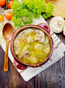 Soup with meatballs, noodles and champignon in a clay bowl on a napkin, parsley, tomatoes, mushrooms and bread on background a wooden board on top