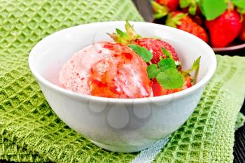 Ice cream strawberry in a white bowl with berries and syrup on a green napkin on a background of a dark wooden board