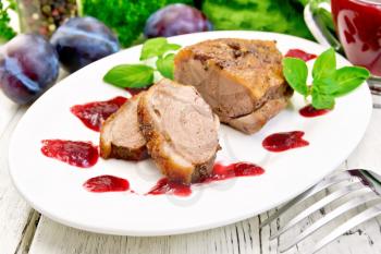 Duck breast with basil and plum sauce in a white oval plate against a light wooden board