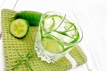 Lemonade with cucumber and rosemary in a glass on a green towel on a wooden plank background