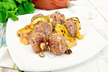 Meatballs baked with zucchini, cheese and nuts in a dish on a towel, parsley on a light wooden board background