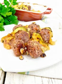 Meatballs baked with zucchini, cheese and nuts in a dish on a towel, parsley on a wooden board background
