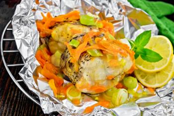 Pike with carrots, leek, basil and slices of lemon in foil on the lattice, a towel on a background of wooden boards