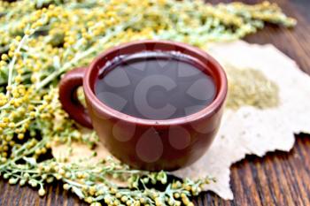 Herbal tea in a brown clay cup, twigs gray sagebrush, wormwood dried on a paper on the background of wooden boards