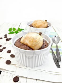 Two white bowl dessert with chocolate and pear, spoon, mint on a kitchen towel on the background light wooden boards