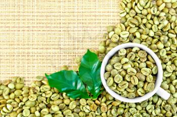 A frame of green coffee beans with leaves and a cup on a yellow coarse woven fabric