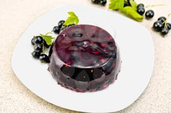 Jelly from a black currant with berries in a plate on a napkin on the background of a granite table