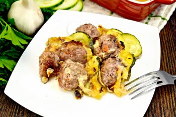 Meatballs baked with zucchini, cheese and nuts in a plate, napkin, garlic, parsley on a background of dark wooden board