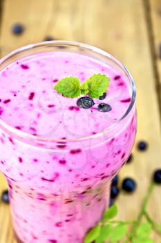 Milk cocktail with blueberries and mint in a glassful, berries and leaves of blueberry on a wooden board background