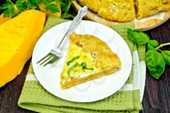 One piece of the pie of pumpkin, salty feta cheese, eggs, cream and herbs in a plate on a napkin, basil on a dark wooden board
