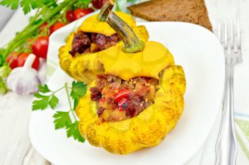 Two yellow squash stuffed with meat, tomatoes and peppers in the dish, bread, garlic, parsley and a napkin on the background light wooden boards