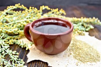 Herbal tea in a clay cup, twigs gray sagebrush, wormwood dried on rough paper on the background of wooden boards