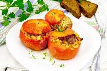 Tomatoes stuffed with meat and steamed wheat bulgur in a plate, napkin, fork, bread and parsley on the background light wooden boards