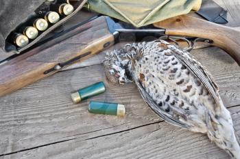 Hunting rifle, bandoleer belt with cartridges, bag and hazel grouse on the background of wooden boards