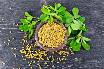 Fenugreek seeds in a bowl with green leaves on a wooden plank background on top