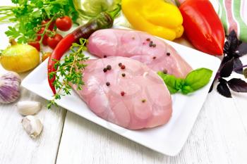 Chicken breast with hot pepper and thyme in a white plate, napkin, parsley and basil, onion, garlic and vegetables against a light wooden board