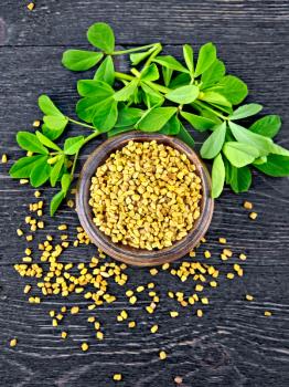 Fenugreek seeds in a bowl and on a table with green leaves on a wooden plank background on top