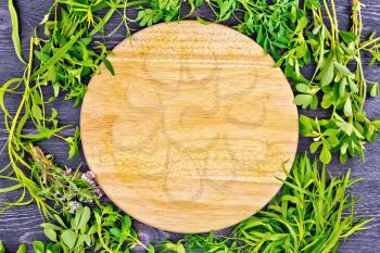 Frame of leaves herbs of fenugreek, rue, savory, tarragon, thyme and round board against the background of a wooden table