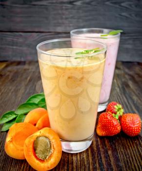 Two tall glasses of milkshake with apricots, strawberries and mint on the background of a wooden board