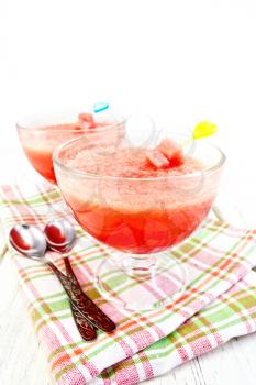 Jelly airy watermelon in two glass bowls, a spoon on a towel on the background of a wooden board