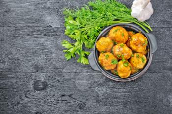 Meatballs with tomato sauce in a brazier with parsley, dill and garlic on a wooden board background on top