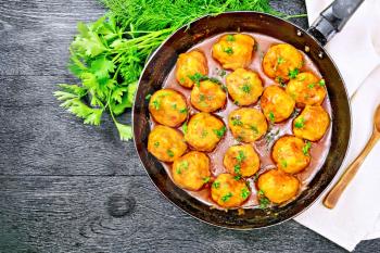 Meatballs with tomato sauce in a frying pan with parsley, dill, napkin and spoon on a black wooden board background