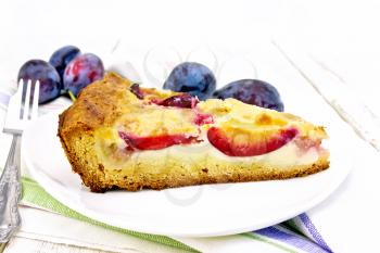 Pie with plums and sour cream in a dish on a towel on a wooden plank background