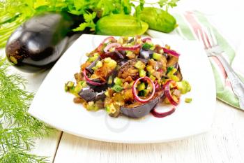 Salad of fried eggplant, fresh and pickled cucumber with red onion, seasoned with vegetable oil and spicy sauce in a plate, napkin, fork and dill on a wooden board background