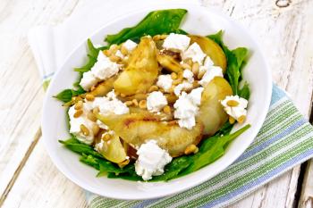 Salad of fried pear, spinach, salted feta cheese and cedar nuts in a plate on a napkin on a light wooden board background