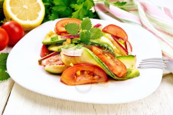 Salad from young zucchini, radish, tomato and mint flavored with lemon juice and soy sauce in a plate, napkin on a light wooden board background