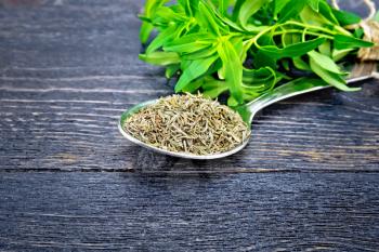 Savory dry in a metal spoon, a bunch of fresh herbs on a background of wooden board