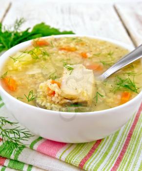 Soup fish kulesh with millet, potatoes and carrots and spoon in a white bowl on a napkin, parsley, dill on a wooden board background