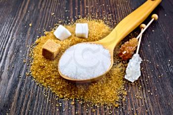 Sugar white and brown in cubes, crystal on a stick and granulated in a spoon on a background of a dark wooden board