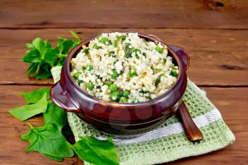 Couscous with spinach and green peas in a clay bowl on a napkin, basil and spoon on a blackboard background