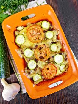 Baked minced meat, tomatoes and zucchini in a brazier on a napkin on the background of a wooden board on top
