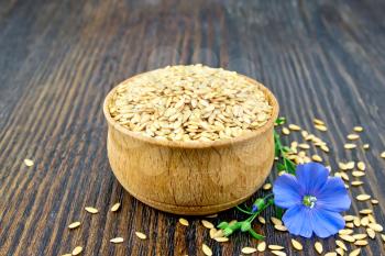 Linen seeds white in a bowl and blue flax flower on a background of a dark wooden board