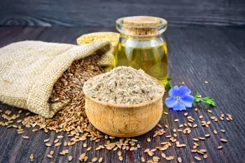 Flax flour in a bowl, seeds in a bag and on a table, blue linen flower and oil in a glass jar on a wooden board background