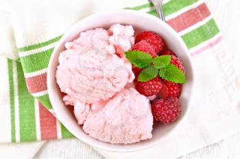 Ice cream crimson with raspberry berries and mint in white bowl, a spoon on towel on wooden board background from above