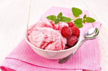 Ice cream crimson with raspberry berries and mint in white bowl, a spoon on pink towel on wooden board background