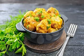 Meatballs with tomato sauce in a brazier, parsley, dill and fork on a wooden plank background