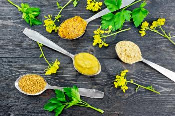 Mustard grainy, powder, seeds and sauce in spoons, yellow mustard flowers and parsley on the background of a wooden board from above