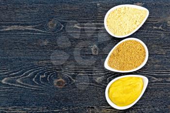 Mustard sauce, seeds and mustard powder in three saucepans on the background of a black wooden board from above