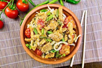 Thai noodles wok with chicken meat, tomatoes, soy sauce and green beans sprinkled with sesame seeds in a plate on a bamboo napkin on a wooden board top background
