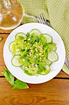 Salad from spinach, fresh cucumbers, rukkola salad, cedar nuts and spring onions, seasoned with vegetable oil on a plate, napkin and fork on the background of the board from above