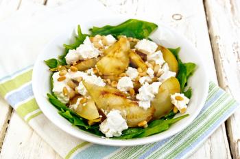 Salad of fried pear, spinach, salted feta cheese and cedar nuts in a plate on a napkin on the background of a wooden board