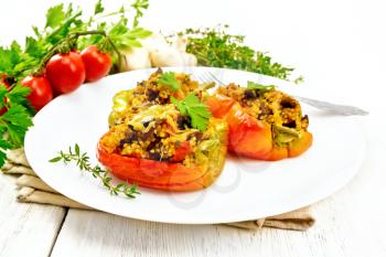 Pepper sweet, stuffed with mushrooms, tomatoes, couscous and cheese in a white plate on a napkin, fork, parsley against the background of wooden board