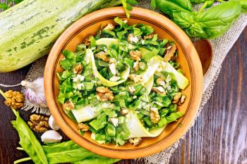 Salad of young zucchini, sorrel, garlic and nuts, seasoned with vegetable oil in a plate on napkin of sackcloth on a background of a dark wooden board on top