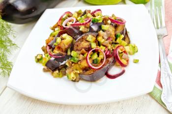 Salad of fried eggplant, fresh and pickled cucumber with red onion, seasoned with vegetable oil and spicy sauce in a plate, towel, fork and dill on a wooden board background
